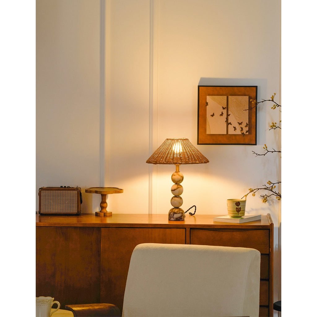 Clérachic rattan lamp lit on a sideboard in a panelled room, with a small framed print above and a cream chair below.
