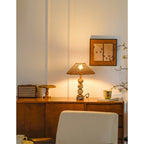Clérachic rattan lamp lit on a sideboard in a panelled room, with a small framed print above and a cream chair below.