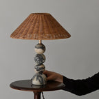 A hand resting on the marble base of this Clérachic table lamp, which stands on a small round wooden side table.