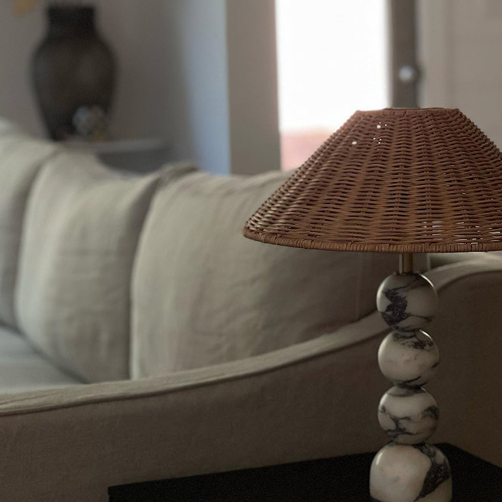 Close view of the marble spheres and rattan shade of this Clérachic lamp beside a linen sofa arm in soft daylight.