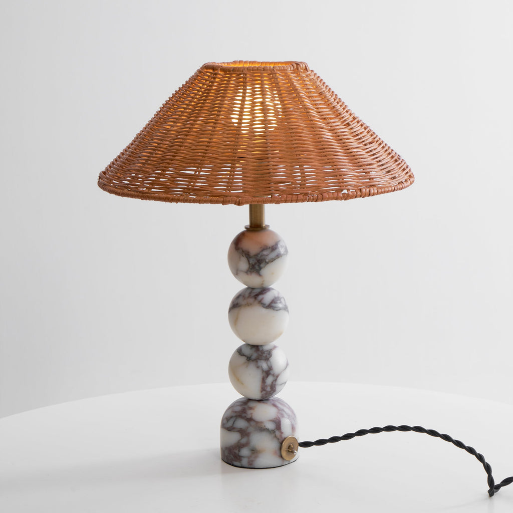 Lit Clérachic table lamp on a white table against a pale grey wall, with a black twisted cord leaving the marble foot.