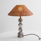 Lit Clérachic table lamp on a white table against a pale grey wall, with a black twisted cord leaving the marble foot.