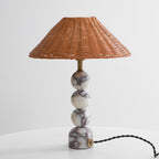 Unlit Clérachic rattan lamp on a white table against a light grey wall, with a black twisted cord trailing from its base.