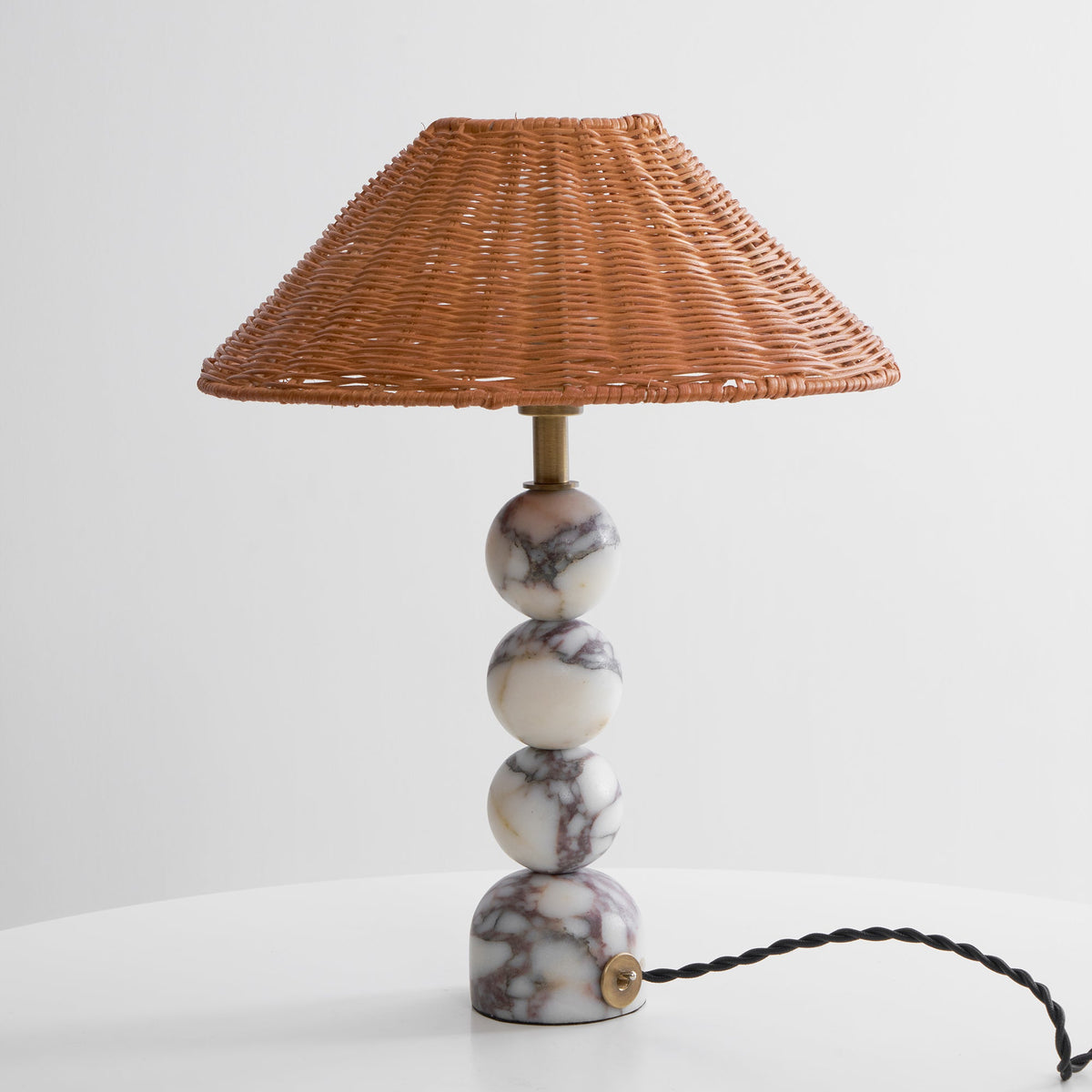 Unlit Clérachic rattan lamp on a white table against a light grey wall, with a black twisted cord trailing from its base.