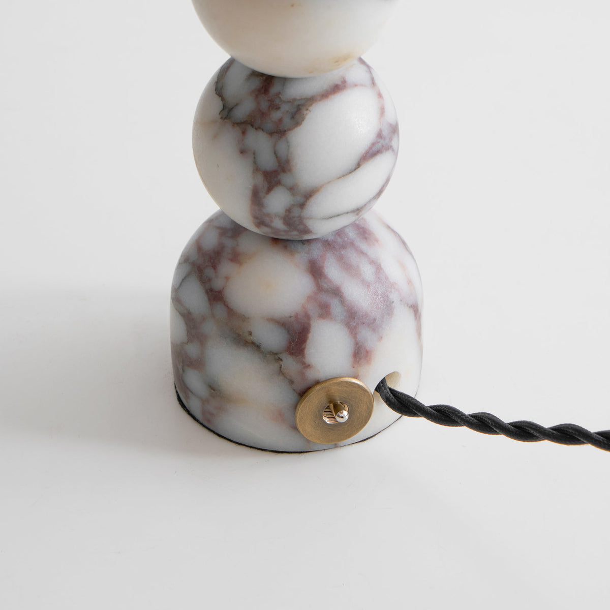 Close view of the marble foot of this Clérachic lamp, with its brass cord entry and black twisted cord.