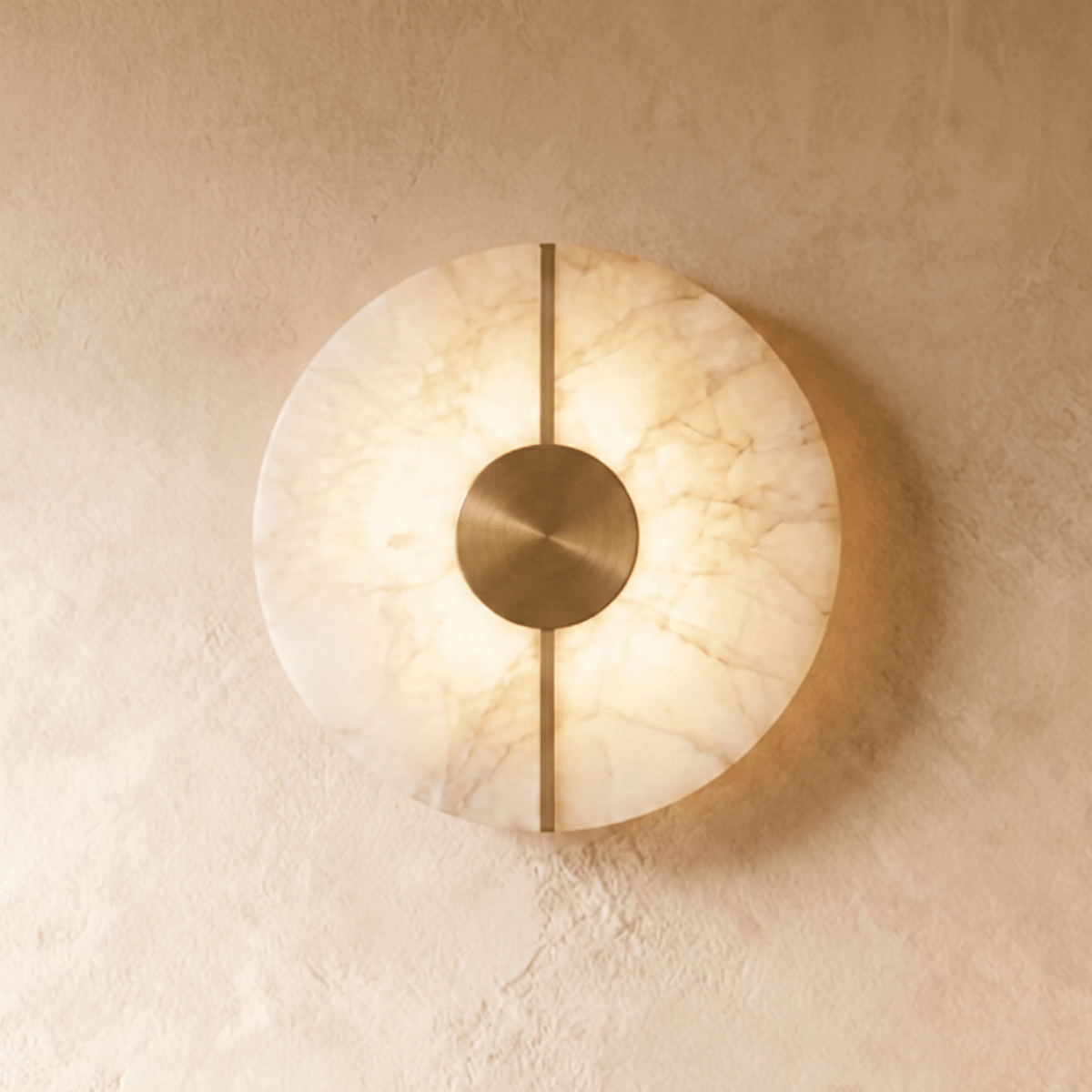 A round Clérachic alabaster wall sconce glows warmly on a plastered wall, its brushed brass disc and bar centered.