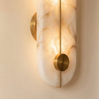 Close-up on the Clérachic sconce's brass mounting disc and center bar set into its glowing alabaster stone body.