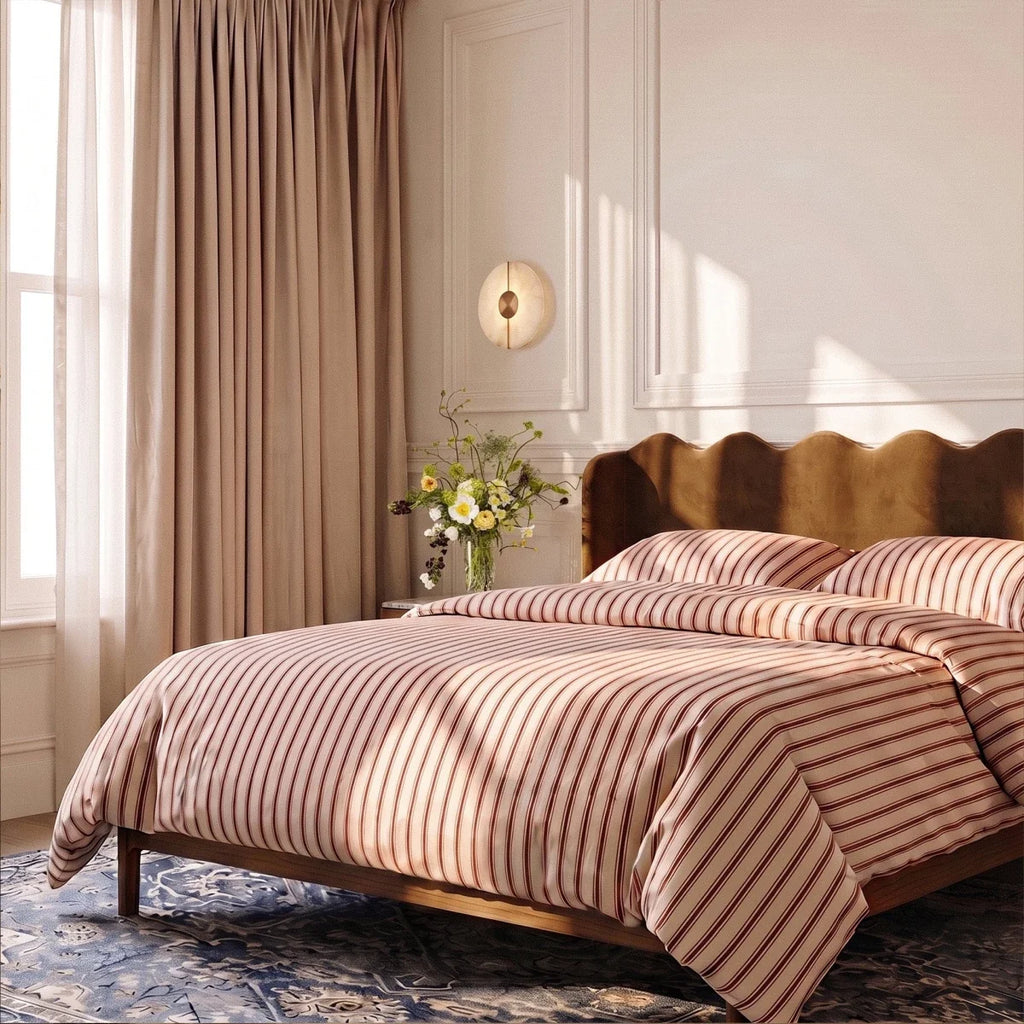 A round Clérachic alabaster sconce warms a paneled bedroom wall beside a striped bed and gathered flowers.