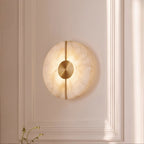 Set into a paneled wall, the round Clérachic alabaster sconce glows softly beside a trailing green plant stem.