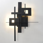 Close view of this Clérachic wall light lit, with a warm glow behind its black panels and through two square cutouts.