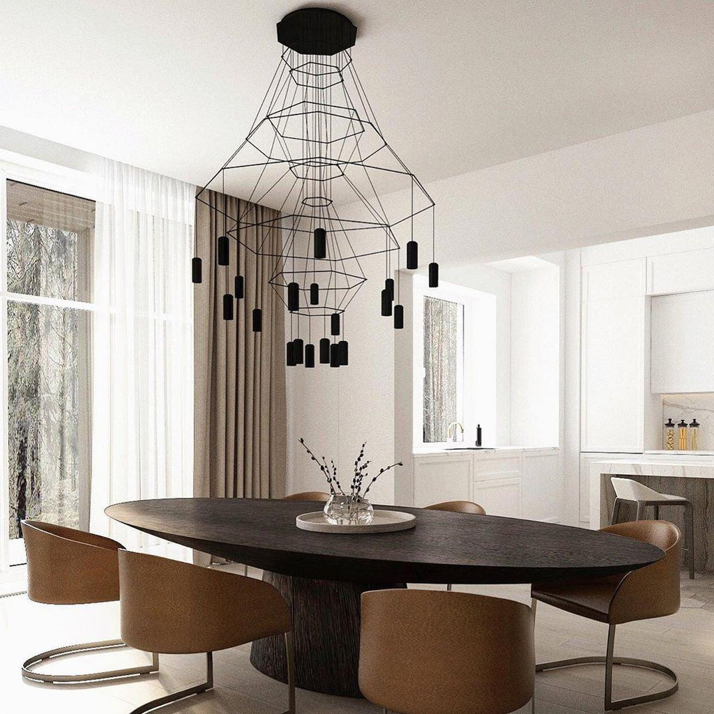 Black Clérachic wire-frame chandelier hung over a dark oval dining table with tan chairs, in a bright kitchen-diner with tall windows.