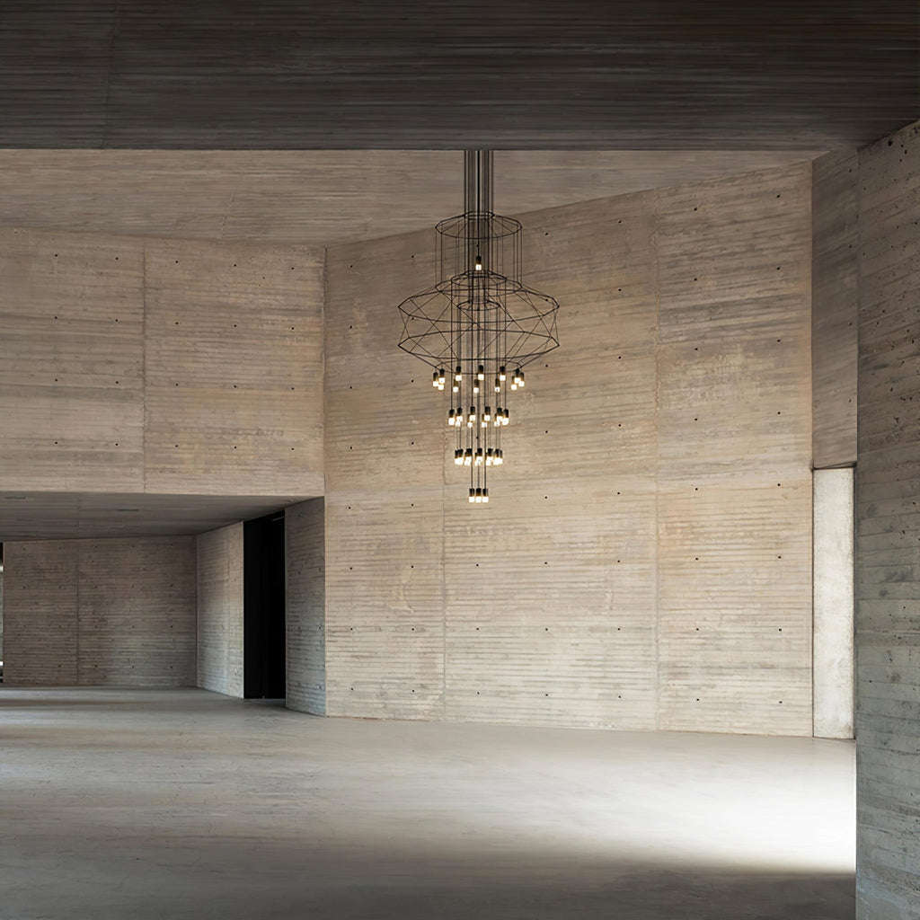 Far view of a Clérachic wire chandelier in a bare board-marked concrete hall, its LED drops lit in a cluster near the bottom.