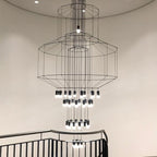 Looking up at a Clérachic chandelier with several octagonal wire frames and many LED drops, seen above a black stair rail.