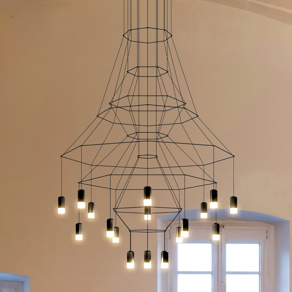 Under-view of the flared Clérachic wire chandelier, its fine black polygon frames narrowing to a lit lower cluster beside a window.