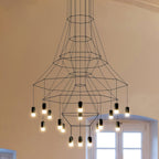 Under-view of the flared Clérachic wire chandelier, its fine black polygon frames narrowing to a lit lower cluster beside a window.