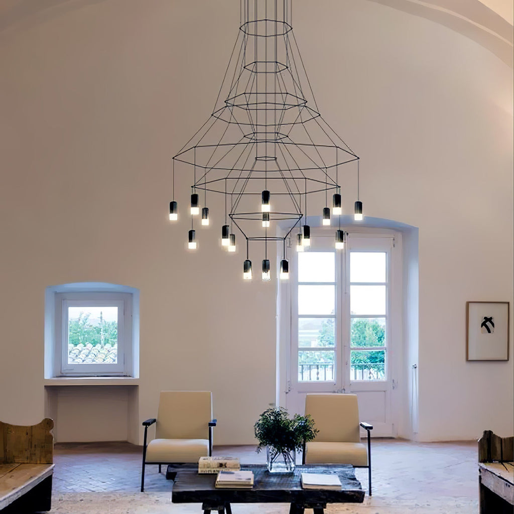 Wire-frame Clérachic chandelier with lit LED terminals, seen above armchairs and a dark coffee table in a vaulted room.