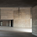 A Clérachic wire chandelier hung high in a raw concrete hall, with its LED drops lit and the floor below left bare.