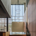 Tall Clérachic wire chandelier running down a glazed stairwell with timber slat walls, its LED drops lit one above another.