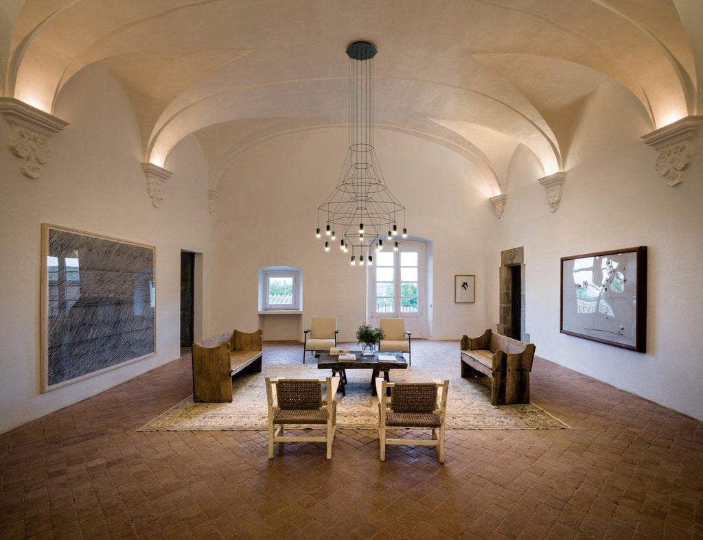 Distant view of a Clérachic wire chandelier in a vaulted hall with a seating group and framed art on both walls.