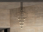 A Clérachic wire chandelier with a lit cluster of LED drops hangs in front of a concrete wall with a pale ceiling.
