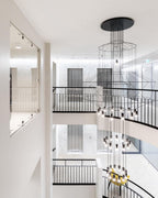 Several levels of a wire chandelier hang down a white stairwell with black balustrades, with a Clérachic LED cluster lit at the foot.