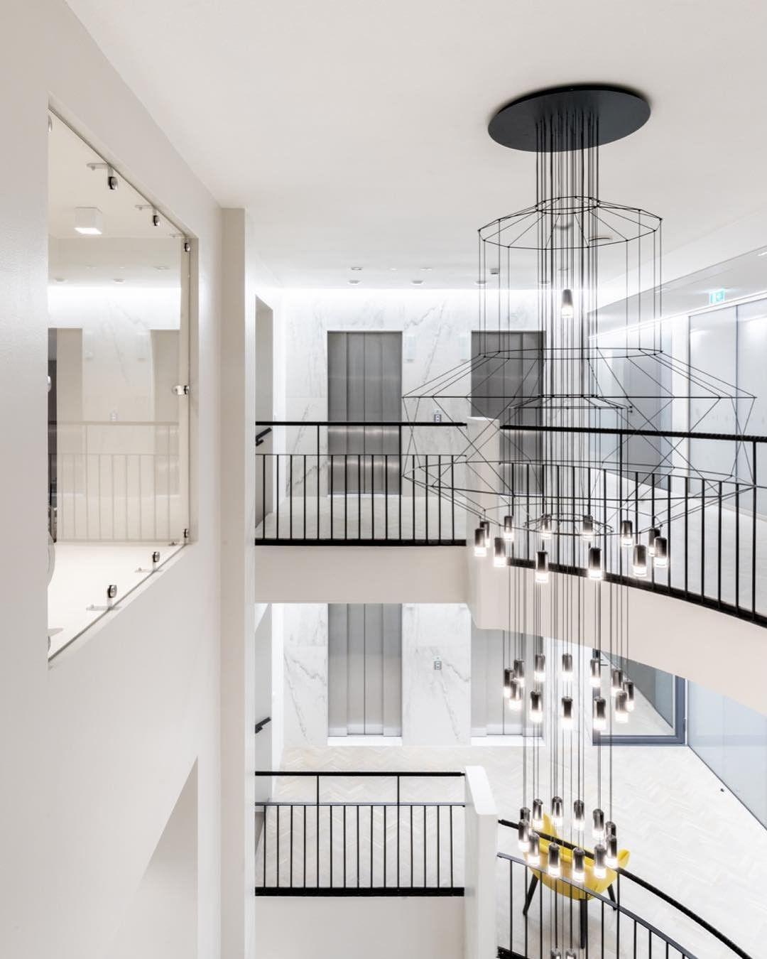 Several levels of a wire chandelier hang down a white stairwell with black balustrades, with a Clérachic LED cluster lit at the foot.