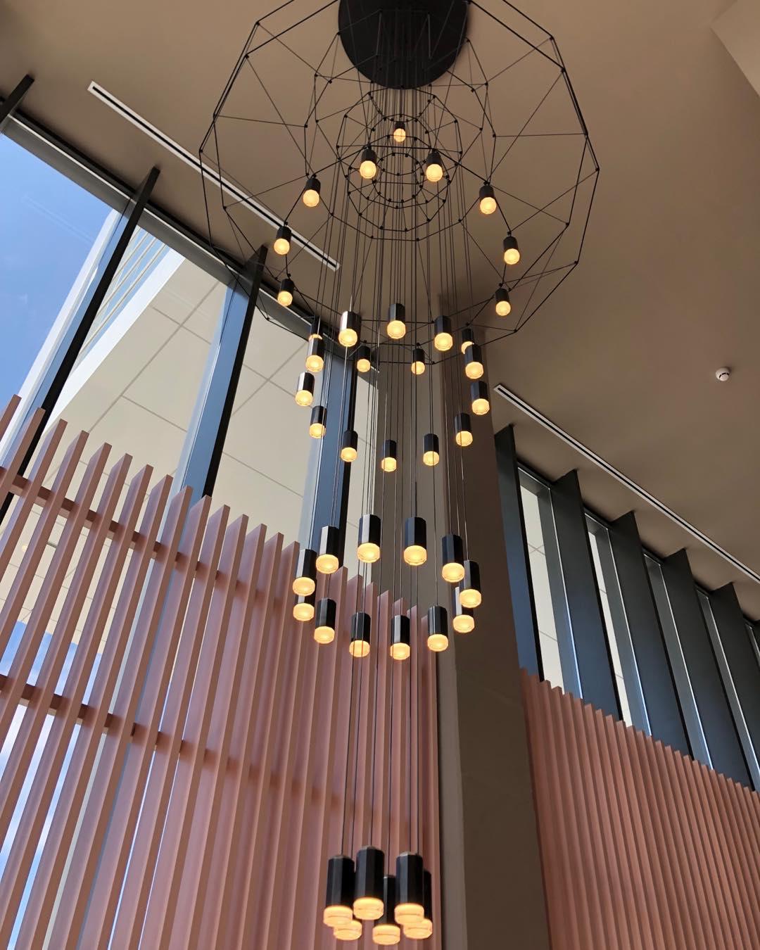 Looking up through the rings of a Clérachic wire chandelier, with its LED terminals glowing warm against a copper-toned slatted wall.