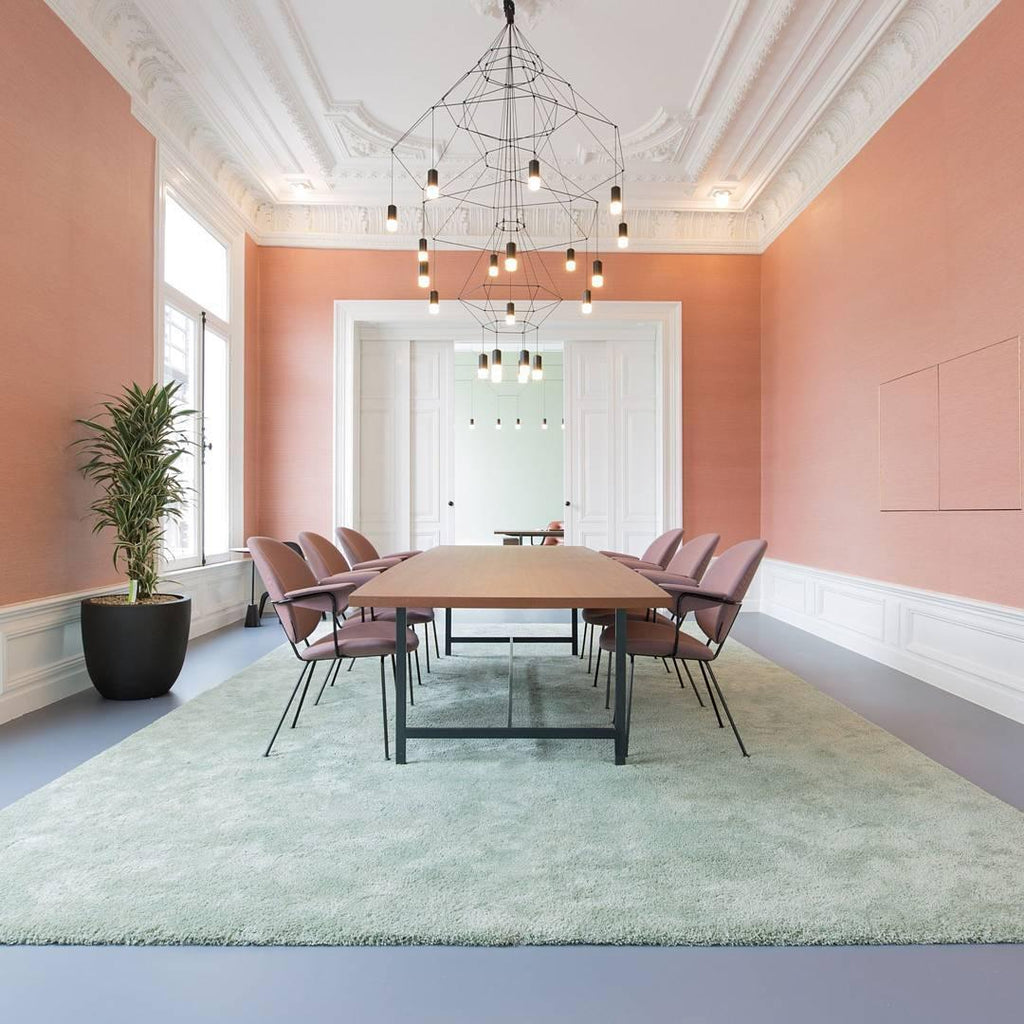 Clérachic wire chandelier hung over a long wooden meeting table in a peach-walled room with plaster cornicing.