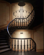 A Clérachic wire chandelier hangs in a dark spiral stairwell with carved black balusters and a warm-lit wall behind.