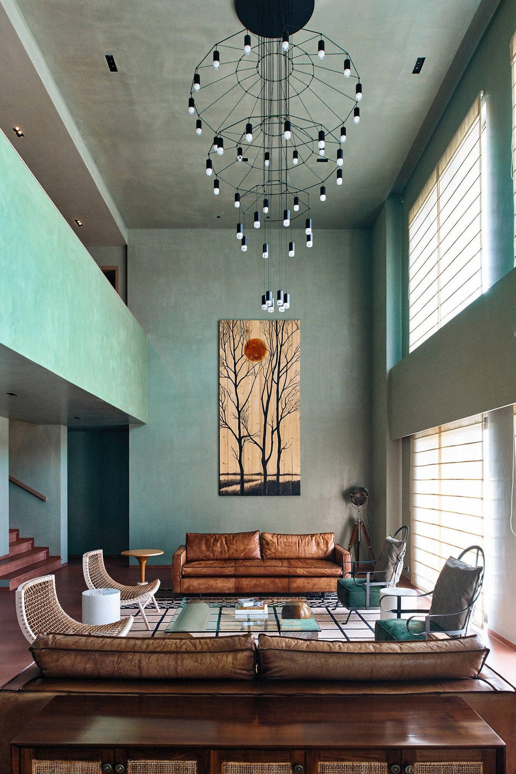 Tall, narrow wire chandelier from Clérachic in a green-walled double-height room, with a leather sofa far below.