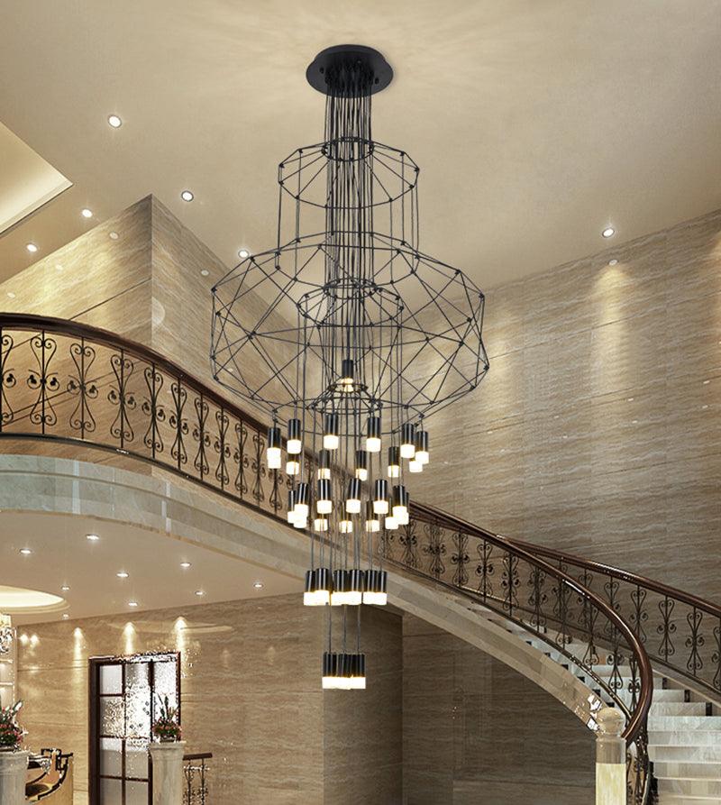 Clérachic wire chandelier with stacked frames hung above a sweeping stair with an ornate iron balustrade and stone walls.