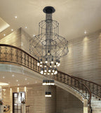 Clérachic wire chandelier with stacked frames hung above a sweeping stair with an ornate iron balustrade and stone walls.