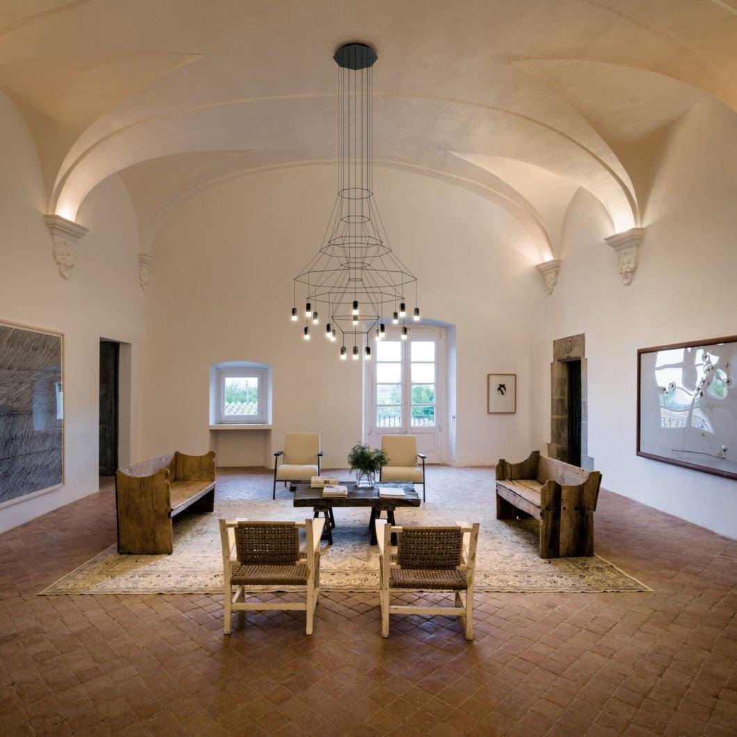 This Clérachic wire chandelier hangs from a vaulted ceiling over a terracotta floor, with wooden benches and a rug below.