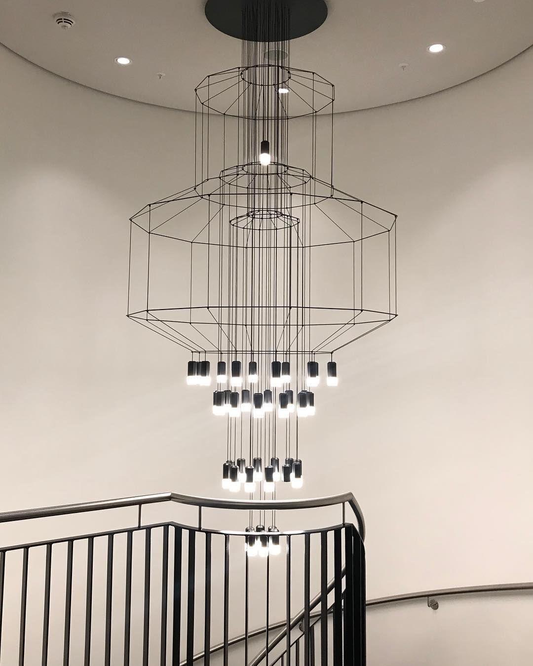 Clérachic wire chandelier seen from below in a round stairwell, with stacked frames, many LED drops and a black handrail.