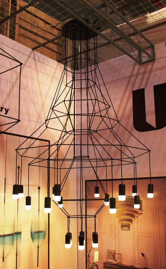 Looking up at a Clérachic wire chandelier with flared frames and lit LED drops in a warm-lit exhibition-style space.