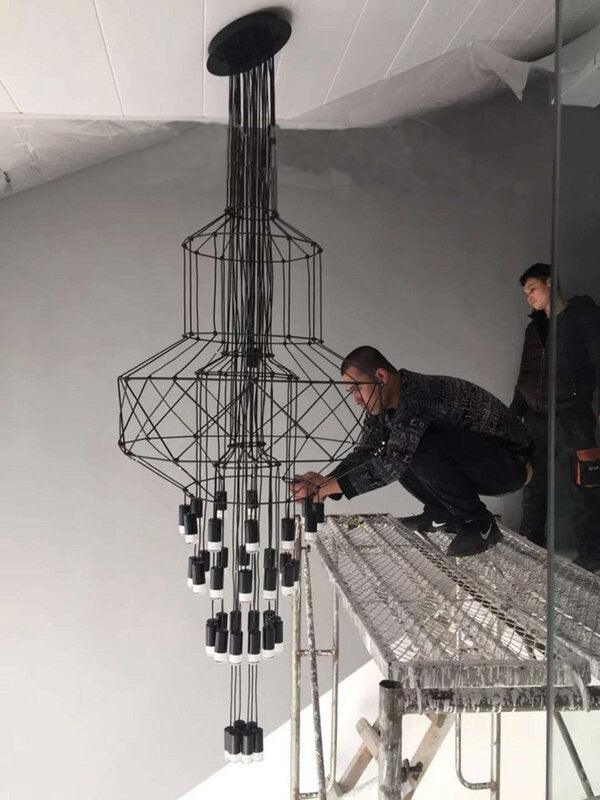 Two people fit a stacked-frame Clérachic wire chandelier from a scaffold platform, with many LED drops already hung.