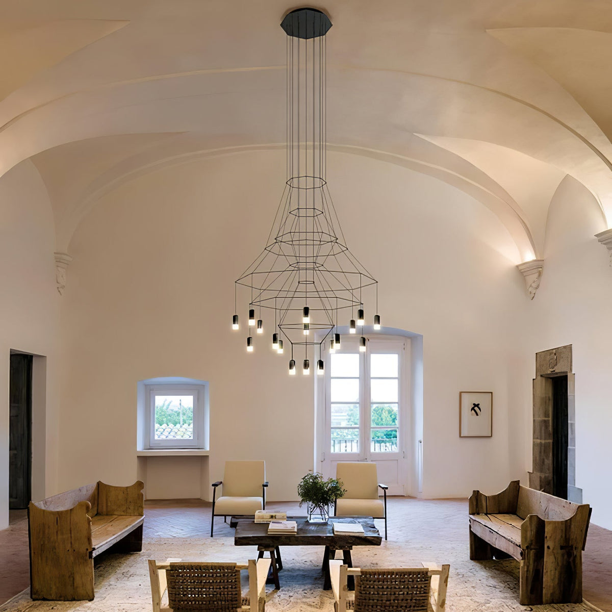 Clérachic chandelier hung in a tall vaulted hall, seen with two wooden benches and a wide coffee table below.