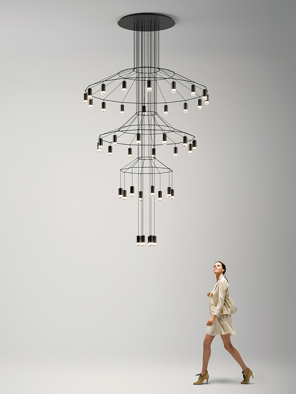A woman walks past a tiered Clérachic wire chandelier on a pale backdrop, which shows its scale against a person.