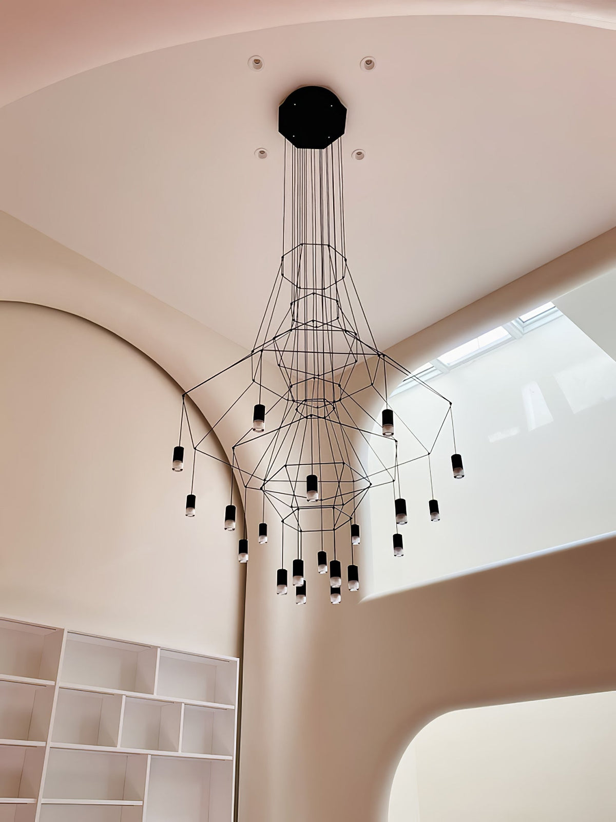 A Clérachic wire chandelier hangs from an octagonal canopy in a curved, rose-toned stairwell next to a white bookcase.