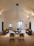 Clérachic chandelier with a cluster of lit LEDs, in a vaulted room with a terracotta floor, a rug and woven chairs.