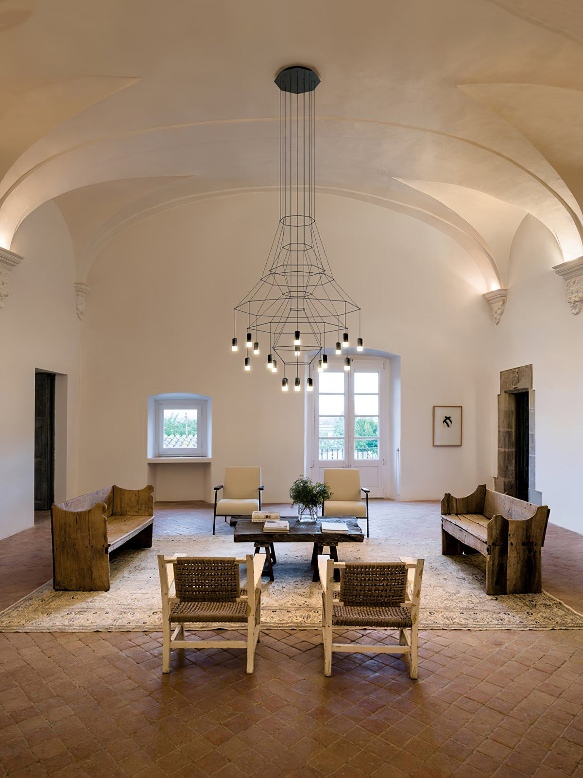 Clérachic chandelier with a cluster of lit LEDs, in a vaulted room with a terracotta floor, a rug and woven chairs.