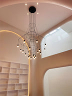 Lit Clérachic wire chandelier hanging by a white bookcase and a curved, softly lit rose-coloured wall.