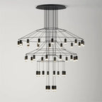 Three tiers of fine black wire and LED drops on this Clérachic chandelier, seen on a light grey wall.