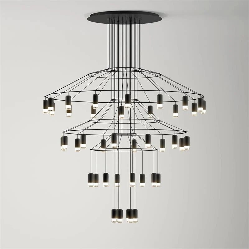Three tiers of fine black wire and LED drops on this Clérachic chandelier, seen on a light grey wall.