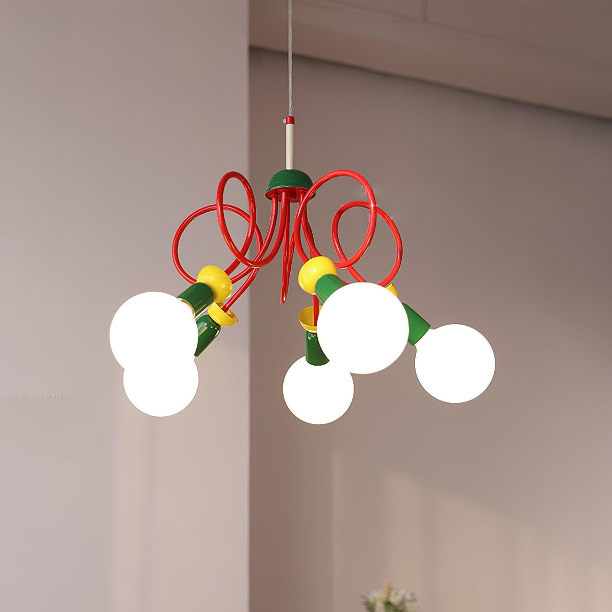 Looping red arms and yellow collars on this Clérachic pendant, seen from the side with its globe bulbs lit near a pale wall.