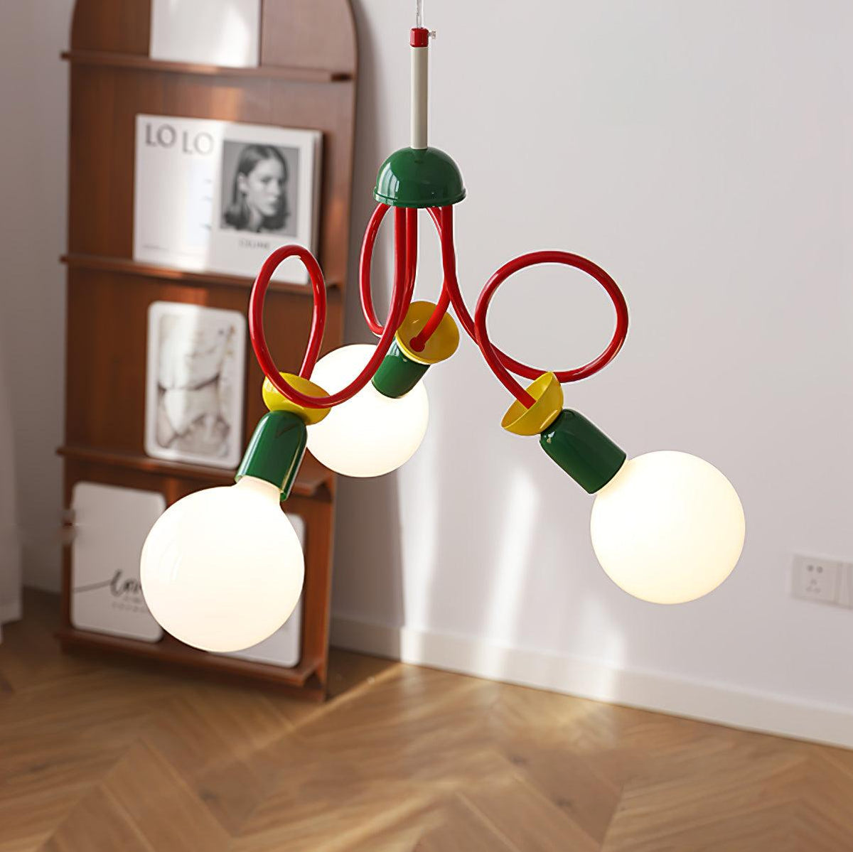 Close angle on three globe bulbs and the red looping arms of this Clérachic pendant, beside a wooden shelf and a herringbone floor.