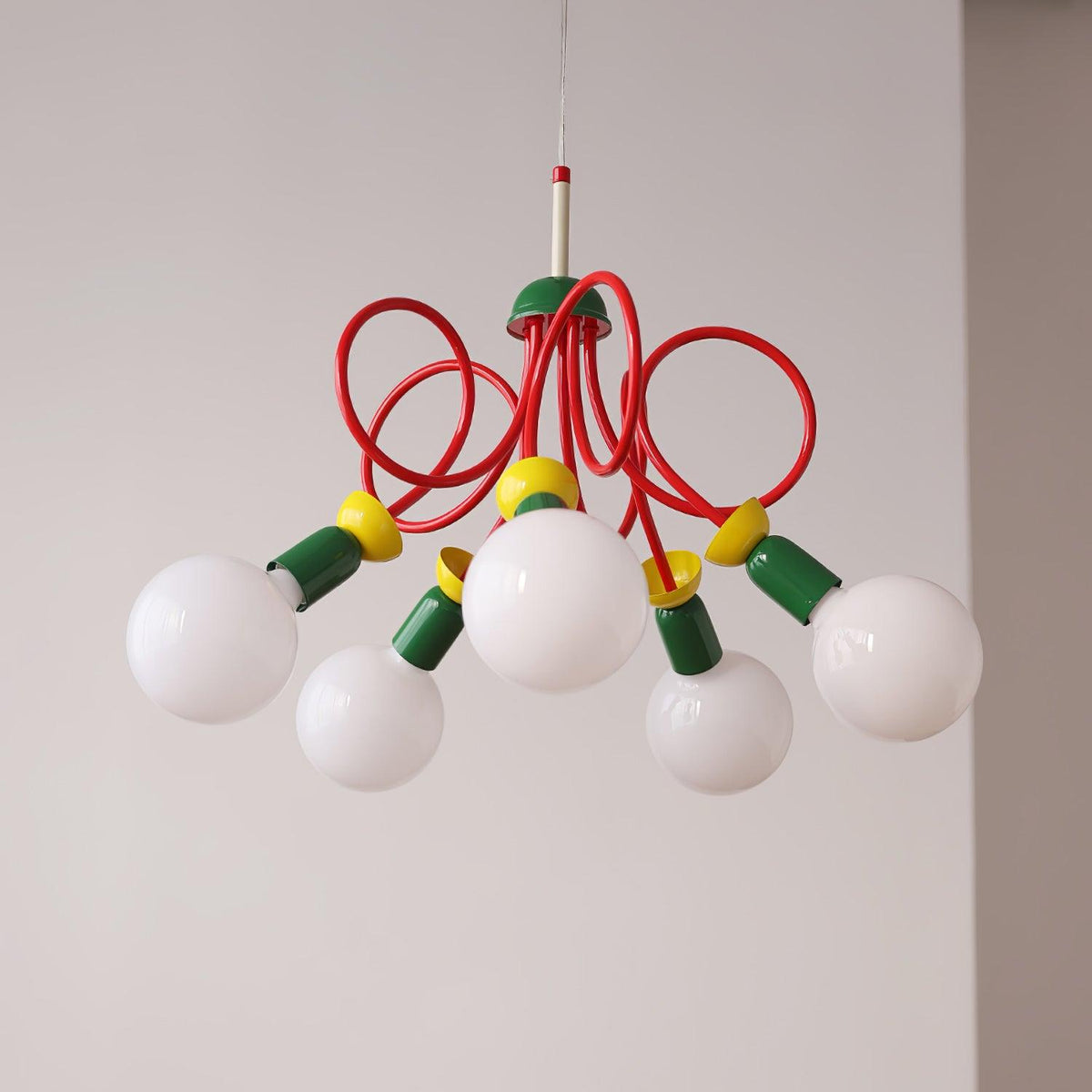 Five white globes hang beneath red looping tubes on this Clérachic pendant, shown against a soft light grey wall.