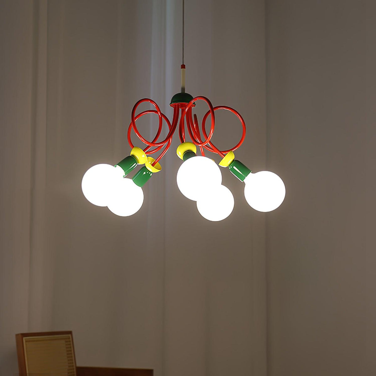 Clérachic pendant switched on in a dim room, its globes glowing and its red loops lit against grey curtains.