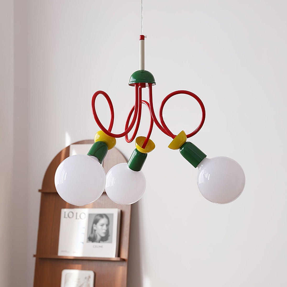 Three globe bulbs and red looping arms of this Clérachic pendant seen close, with an arched shelf and book display behind.