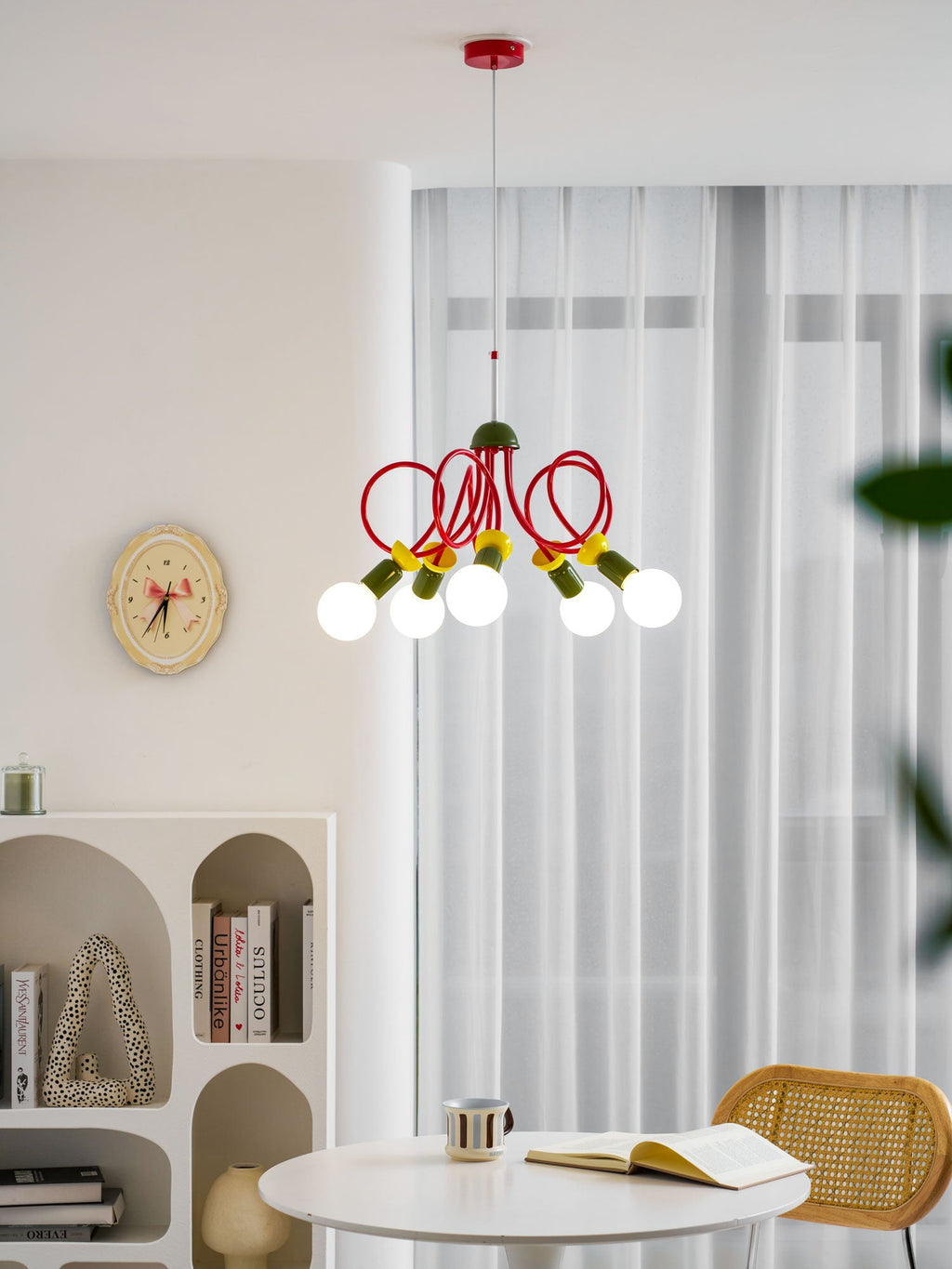 This Clérachic pendant hangs by sheer curtains, with a round wall clock, arched shelving and a cane chair below it.